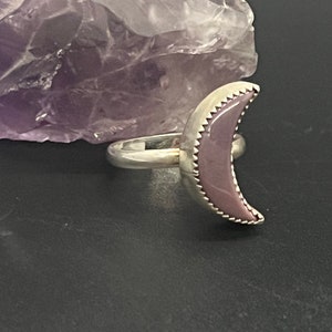 May include: A silver ring with a purple crescent moon shaped stone.