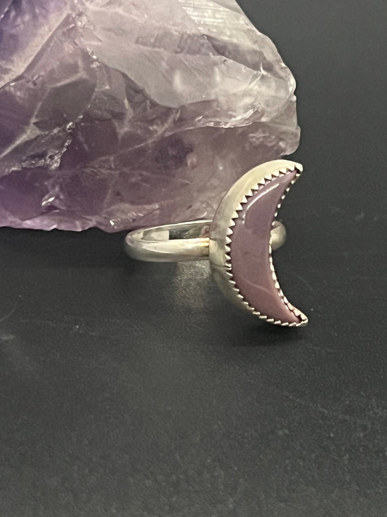 May include: A silver ring with a purple crescent moon shaped stone.