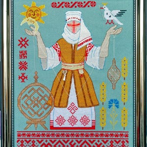 May include: Framed cross-stitch artwork depicting a figure in traditional dress, holding a sun and a bird. The design incorporates geometric patterns in red, white, and gold on a teal background. The frame is gold.