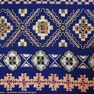 May include: Close-up of blue fabric with detailed embroidery. The design features geometric patterns in white, green, pink, and gold. The embroidery includes floral and diamond shapes, creating a textured surface.