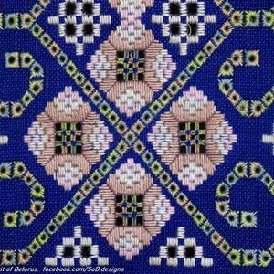 May include: A close-up of a blue fabric with a detailed cross-stitch pattern. The design features geometric shapes in white, pink, black, and green, creating a symmetrical and intricate design. The text "Spirit of Belarus" is visible at the bottom.