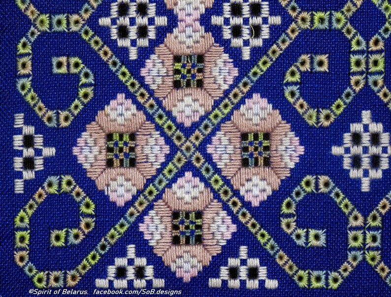 May include: A close-up of a blue fabric with a detailed cross-stitch pattern. The design features geometric shapes in white, pink, black, and green, creating a symmetrical and intricate design. The text "Spirit of Belarus" is visible at the bottom.