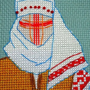 May include: Cross-stitch embroidery of a person wearing a white head covering with red accents and a red cross design on the face. The person is wearing a yellow and brown patterned garment. The background is a light teal colour.