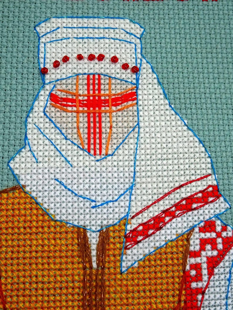 May include: Cross-stitch embroidery of a person wearing a white head covering with red accents and a red cross design on the face. The person is wearing a yellow and brown patterned garment. The background is a light teal colour.