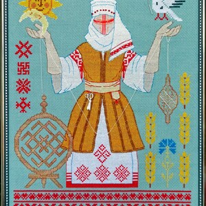 May include: Framed cross-stitch artwork depicting a central figure in traditional dress, holding objects connected by threads. The figure is surrounded by symbolic elements, including a sun, a bird, and geometric patterns. The color palette includes gold, red, white, and blue.