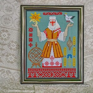 May include: Framed cross-stitch artwork depicting a woman in traditional dress holding a sun and a dove. The design incorporates geometric patterns in red, yellow, and white on a teal background. The frame is silver.