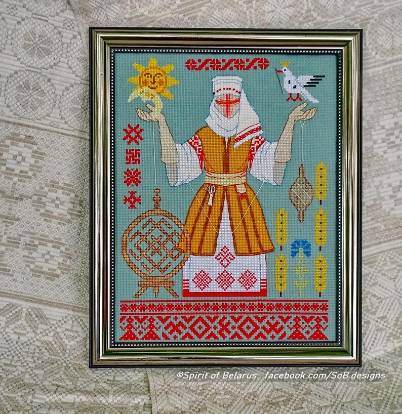 May include: Framed cross-stitch artwork depicting a woman in traditional dress holding a sun and a dove. The design incorporates geometric patterns in red, yellow, and white on a teal background. The frame is silver.