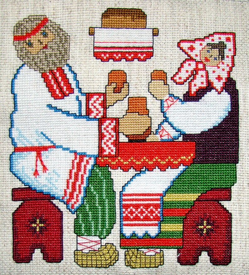 May include: Cross-stitch embroidery depicting a man and woman in traditional clothing sitting at a table with a loaf of bread. The man is wearing a white shirt with red and white embroidery, and the woman is wearing a white shirt with red and white embroidery and a red and white headscarf.