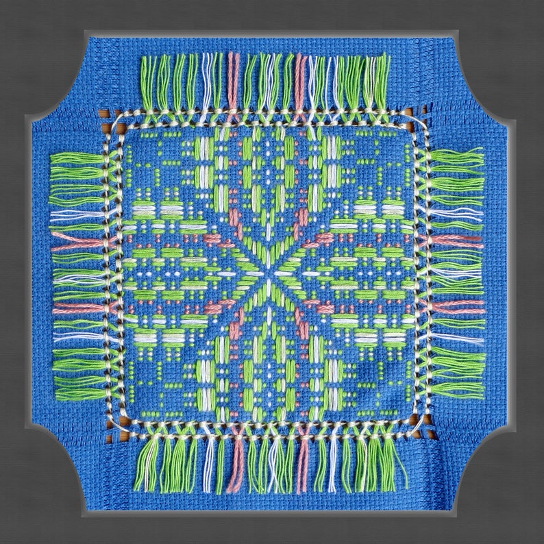 May include: A blue square with a white, green, and pink cross-stitch design. The design is surrounded by a fringe of white, green, and pink threads.