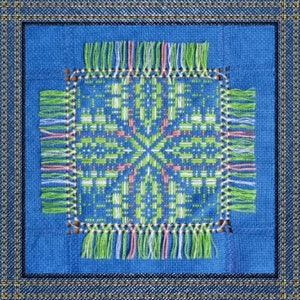May include: A blue square with a green, white, and pink embroidered design. The design is surrounded by a fringe of green, white, and pink threads.