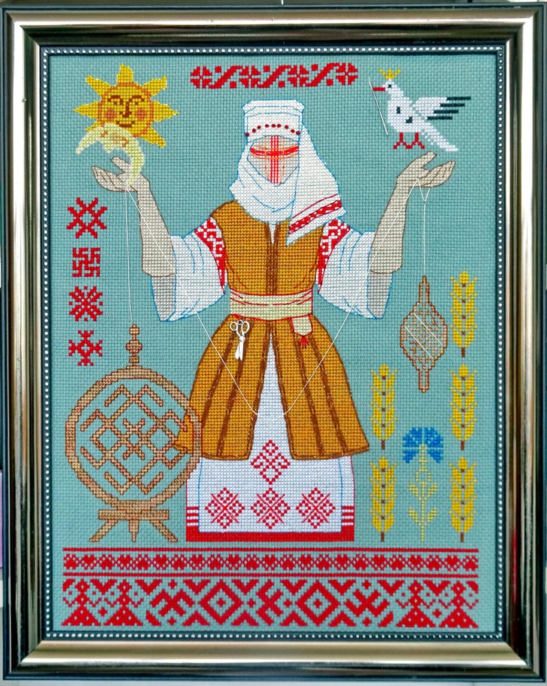 May include: Framed cross-stitch artwork depicting a figure in traditional dress, holding a sun and a bird. The design incorporates geometric patterns in red, white, and gold on a teal background. The frame is gold.