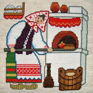 May include: A cross-stitch embroidery depicting a woman in traditional clothing standing in front of a white brick oven. The woman is holding a wooden spoon and there is a basket of bread in front of the oven.