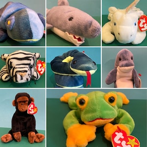 Puede incluir: Una colección de diez peluches, incluyendo un lagarto azul y amarillo, un tiburón gris, un unicornio blanco, una cebra blanco y negro, una serpiente azul, un delfín morado, una rana verde y un gorila negro. Cada peluche tiene una etiqueta roja con la palabra "TY" en ella.