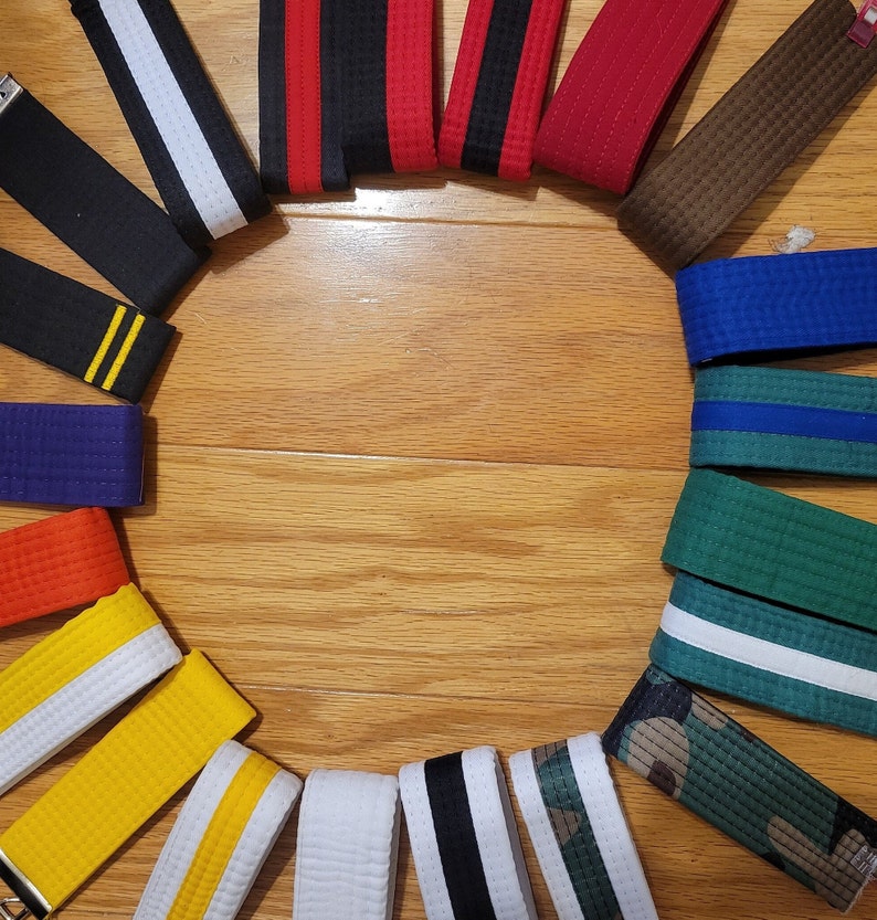 May include: A collection of martial arts belts arranged in a circle on a wooden surface. The belts are in various colors, including black, white, red, blue, green, brown, and yellow.