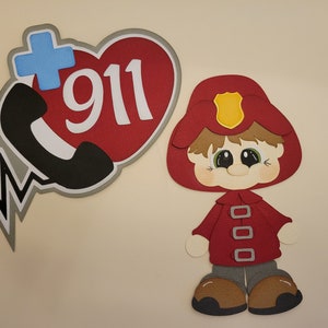 May include: A red heart with a white plus sign and the number 911 inside. A black phone receiver is attached to the heart. A black and white EKG line is below the heart. A cartoon firefighter with a red hat and jacket is standing to the right of the heart.