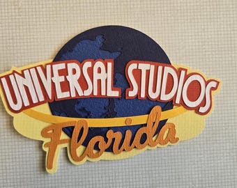 May include: A colorful Universal Studios Florida logo. The design features the words "UNIVERSAL STUDIOS" in white letters with a red outline, and "Florida" in orange script. A blue globe is in the background.