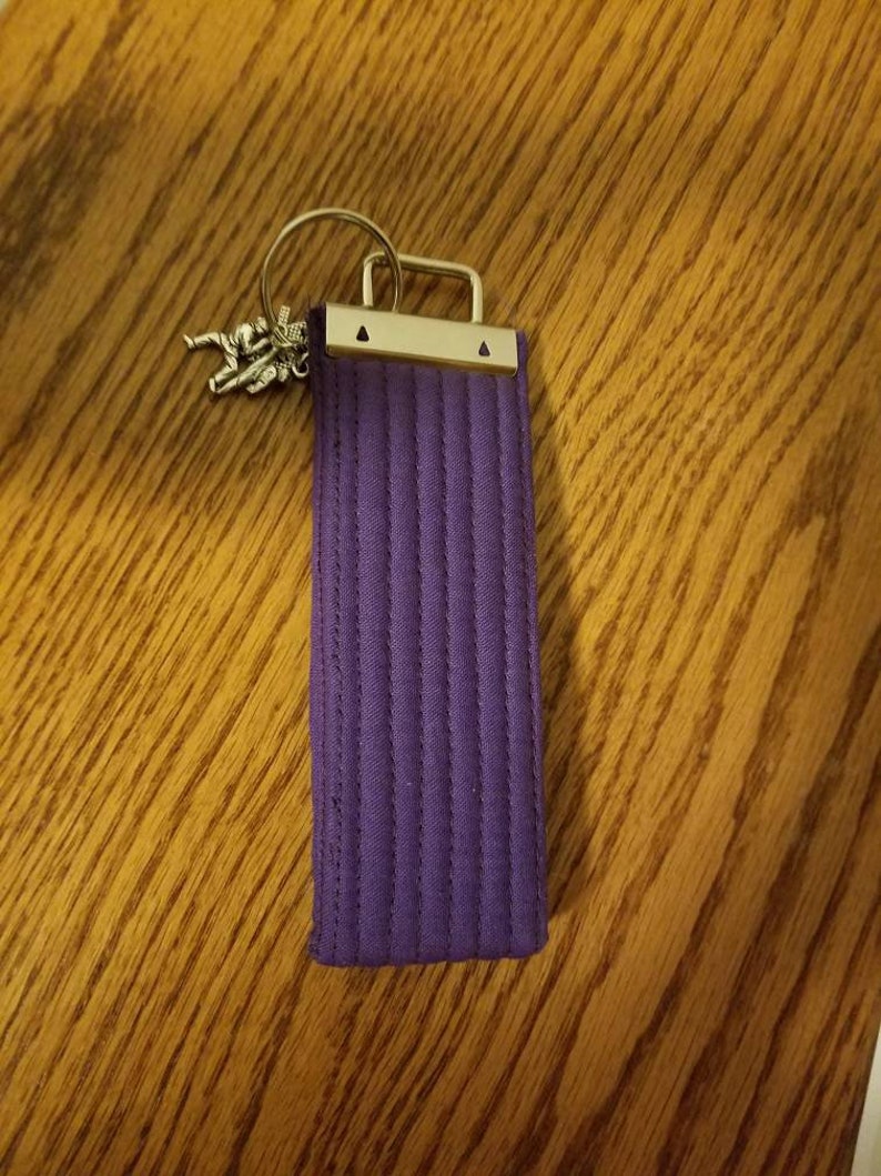 May include: A purple fabric belt with a silver buckle and a small silver charm attached to a key ring.