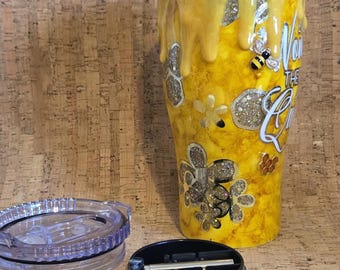May include: A yellow tumbler with a bee-themed design. The tumbler features a dripping honey effect, glitter accents, and the text "You're the Queen Bee". Includes a clear lid and a black lid.