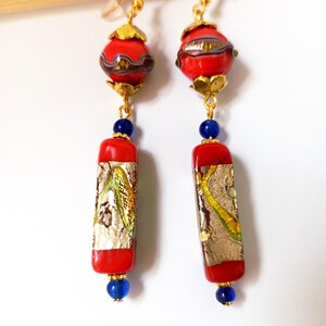 May include: A pair of long, red and gold earrings with blue beads. The earrings feature a round, red bead with gold accents and a long, rectangular red bead with gold and silver details.