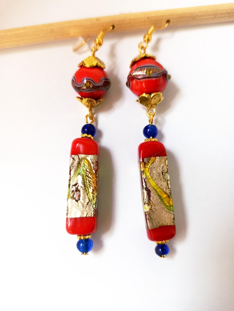 May include: A pair of long, red and gold earrings with blue beads. The earrings feature a round, red bead with gold accents and a long, rectangular red bead with gold and silver details.