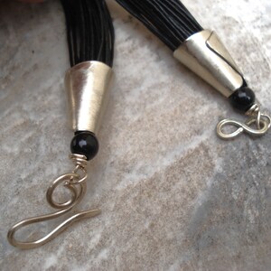 May include: A black leather cord necklace with silver end caps and black beads. The necklace has a silver lobster clasp.