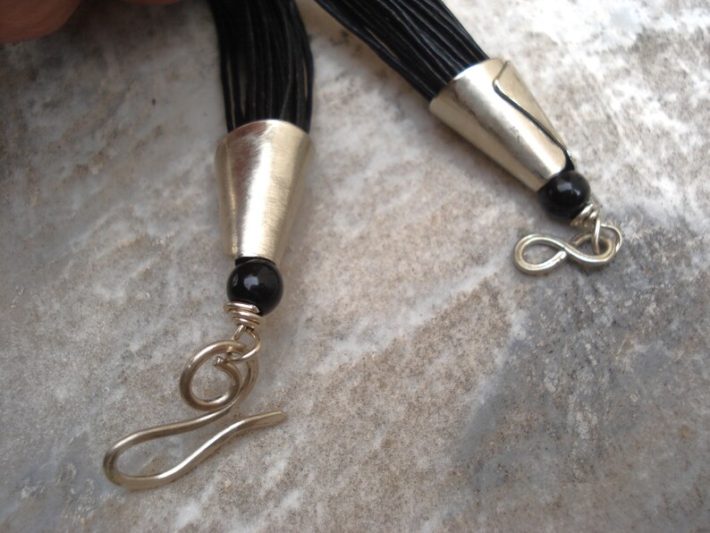 May include: A black leather cord necklace with silver end caps and black beads. The necklace has a silver lobster clasp.