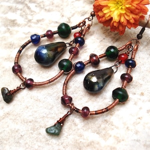 以下が含まれることがあります： 虹色の涙型のガラスビーズ、紫、緑、赤のガラスビーズ、緑の石のアクセントが付いた銅線イヤリングです。