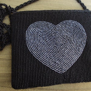 Puede incluir: Un bolso de noche negro de cuentas con un dise&ntilde;o de coraz&oacute;n plateado. El bolso tiene una larga correa negra de cuentas.