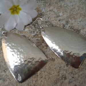 May include: A pair of silver hammered earrings with a teardrop shape. The earrings are made of a smooth, shiny metal and have a textured surface.