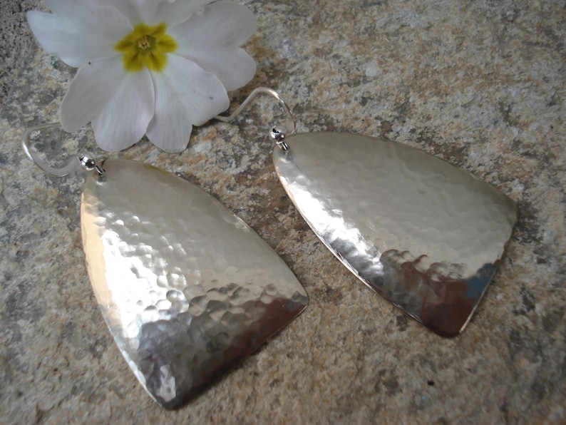 May include: A pair of silver hammered earrings with a teardrop shape. The earrings are made of a smooth, shiny metal and have a textured surface.