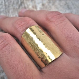 May include: A wide gold hammered metal ring. The ring is thick and has a textured surface.