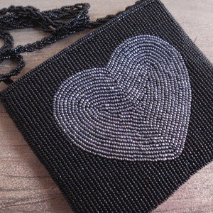 Puede incluir: Un bolso de noche negro de cuentas con un dise&ntilde;o de coraz&oacute;n plateado. El bolso tiene una correa de cadena.