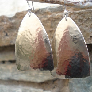 May include: A pair of silver hammered teardrop earrings. The earrings are made of hammered metal and have a textured surface.