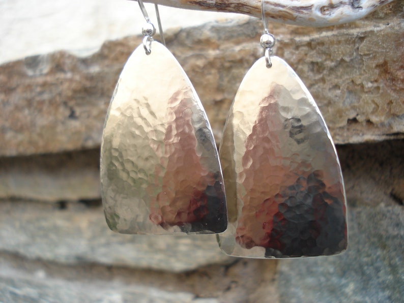 May include: A pair of silver hammered teardrop earrings. The earrings are made of hammered metal and have a textured surface.