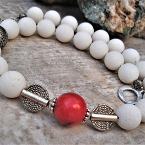 May include: A white lava rock beaded necklace with silver accents and a single red coral bead.