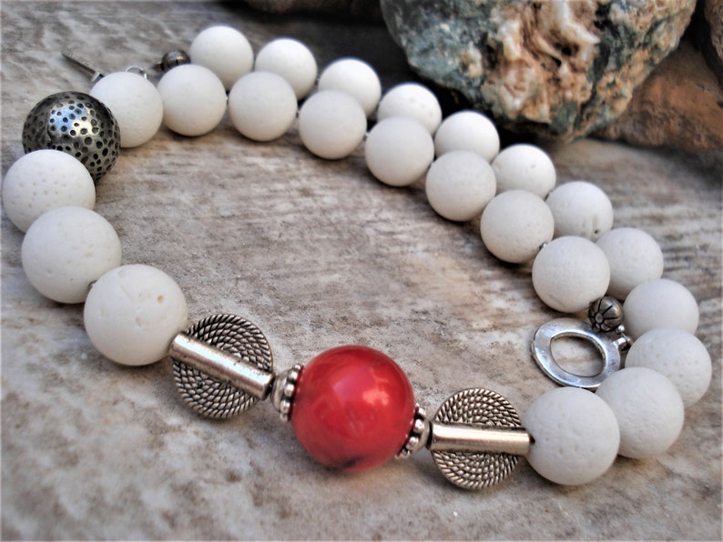 May include: A white lava rock beaded necklace with silver accents and a single red coral bead.