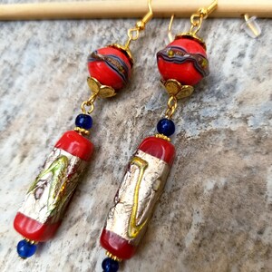 May include: A pair of long, dangling earrings with red and gold glass beads. The beads are patterned with gold and silver leaf. The earrings have blue glass beads at the bottom.