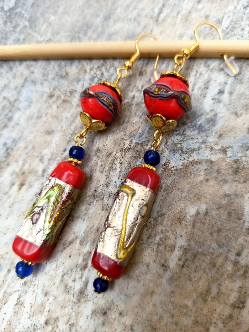 May include: A pair of long, dangling earrings with red and gold glass beads. The beads are patterned with gold and silver leaf. The earrings have blue glass beads at the bottom.