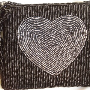 Puede incluir: Un bolso de noche negro de cuentas con un dise&ntilde;o de coraz&oacute;n plateado.