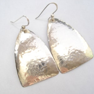 May include: A pair of silver hammered earrings with a triangular shape. The earrings have a textured surface and a simple design.