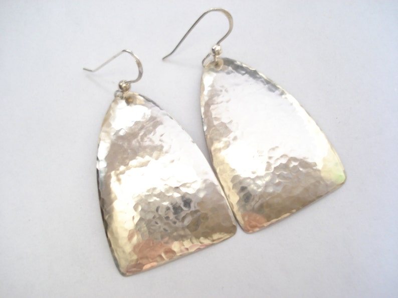 May include: A pair of silver hammered earrings with a triangular shape. The earrings have a textured surface and a simple design.