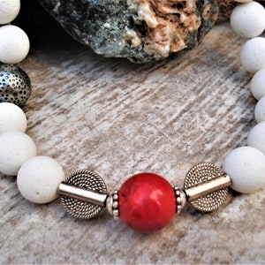 May include: White lava rock beads with silver spacers and a red coral bead in the center.