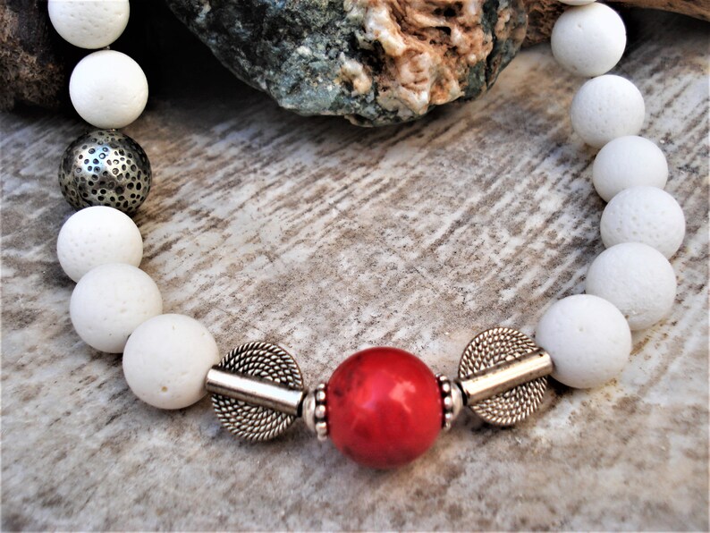 May include: White lava rock beads with silver spacers and a red coral bead in the center.