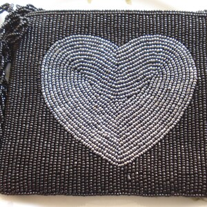 Puede incluir: Un bolso de noche negro de cuentas con un dise&ntilde;o de coraz&oacute;n plateado.