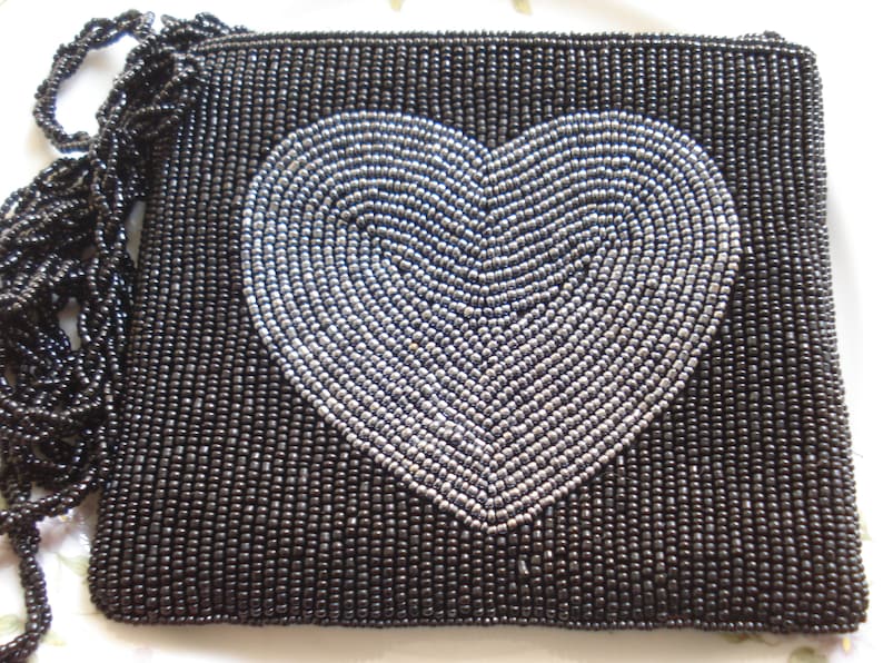 Puede incluir: Un bolso de noche negro de cuentas con un dise&ntilde;o de coraz&oacute;n plateado.