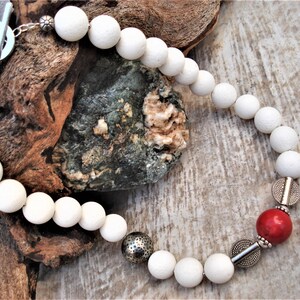 May include: White bead necklace with silver accents and a single red bead. The necklace has a toggle clasp.