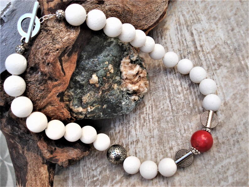 May include: White bead necklace with silver accents and a single red bead. The necklace has a toggle clasp.