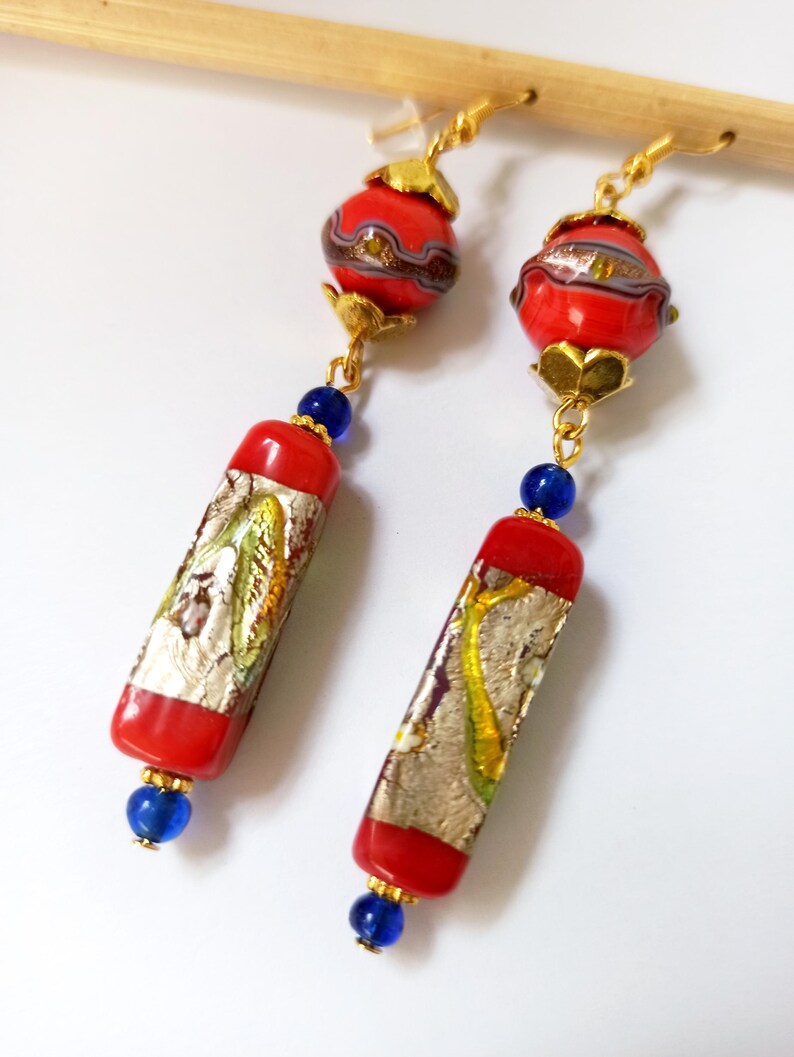 May include: Red and gold dangle earrings with a round and rectangular glass bead design. The beads have a silver and gold foil pattern.