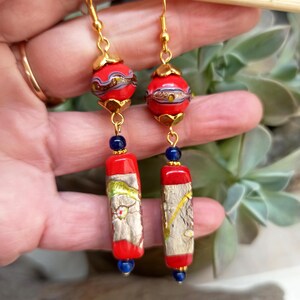 May include: Gold dangle earrings with red and gold patterned glass beads and blue glass beads.