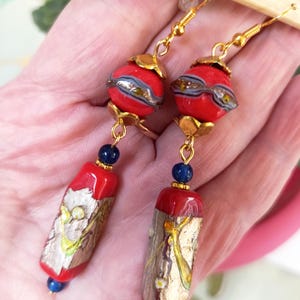May include: A pair of dangle earrings with red and gold glass beads and blue accents. The beads are decorated with gold leaf and a floral pattern.